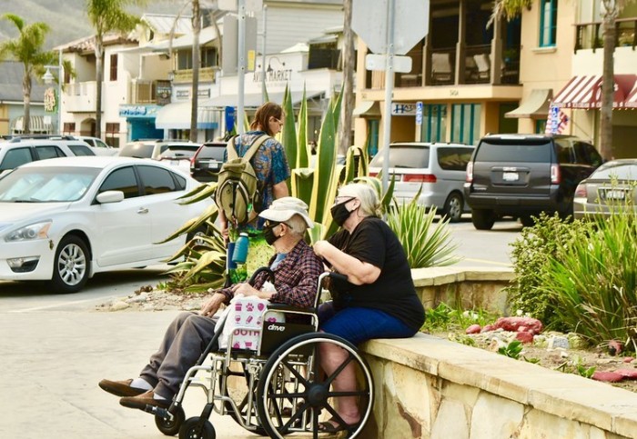 Elderly couple rest in the street wearing face masks to protect them from wildfire smoke in Avila Beach, California (CC-BY-2.0)