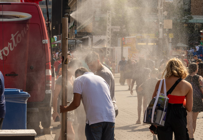 Fully dressed people walking under water mist spray system to cool off in a sunny street during a heatwave