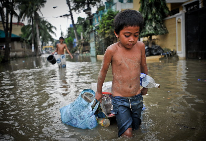 Boy dragging plastic bags and bottles through floodwater
