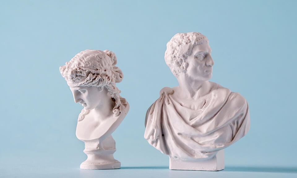 Two white Roman or Grecian antique style busts of young people over a blue background