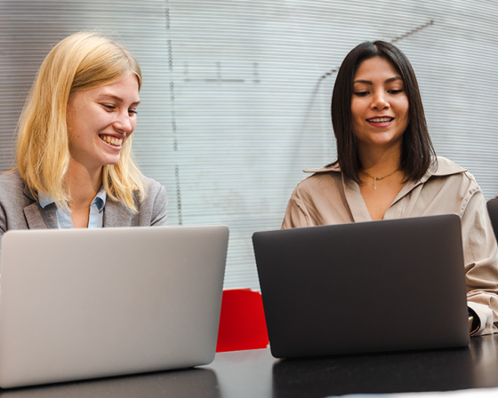 Two female students smiling with laptops