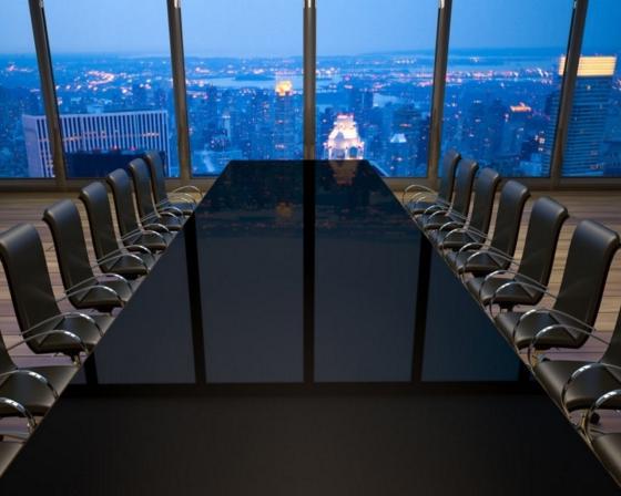 An empty boardroom with a city skyline at night beyond the window