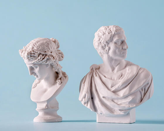 Two white Roman or Grecian antique style busts of young people over a blue background