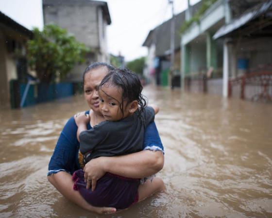 A woman carries a child through a flooded urban street