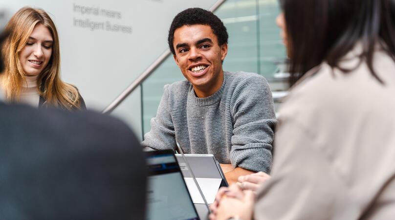 A young male student smiling while in a meeting with his two female peers