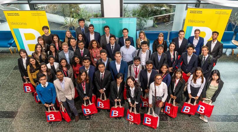 A group of student in the Imperial College Business School building holding red IB tote bags