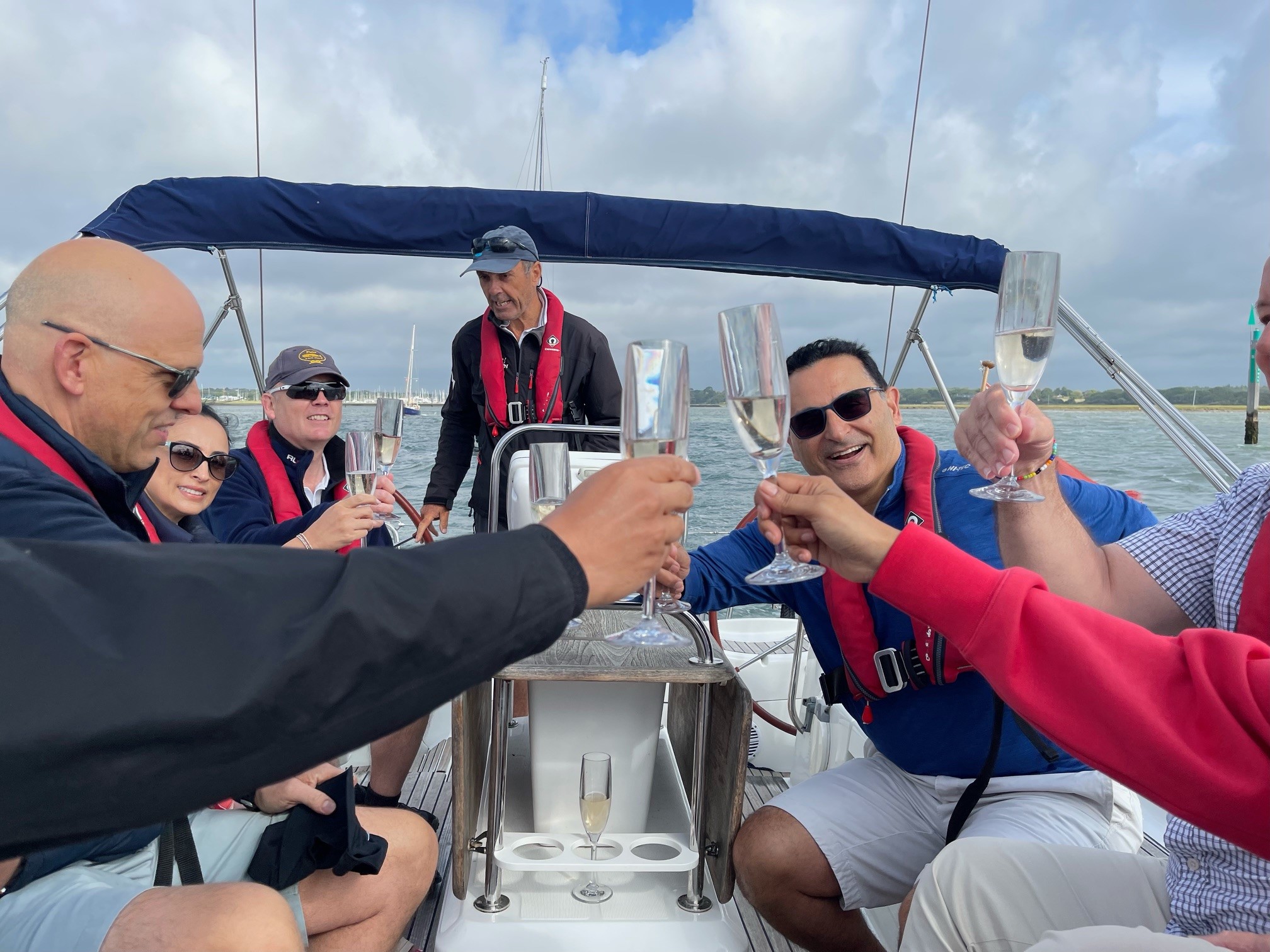 Alumni on a boat in Hampshire toasting their reunion with prosecco or champagne. They are wearing life jackets.