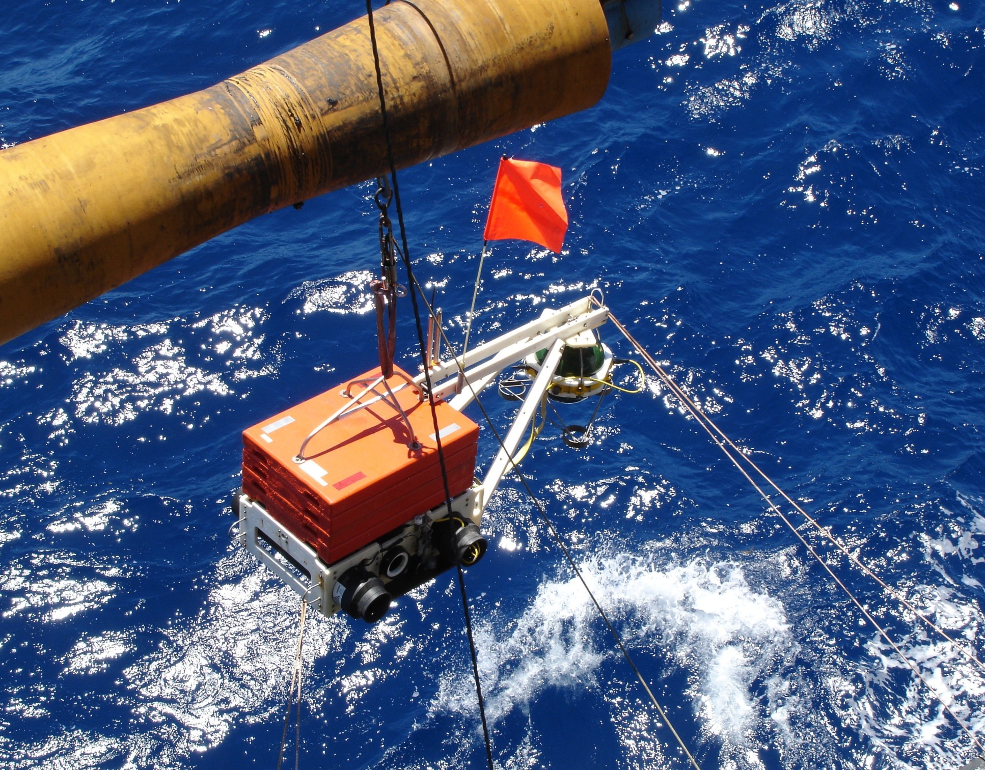 A photo of a seismometer, in a large orange box, being deployed into the sea from a research vessel