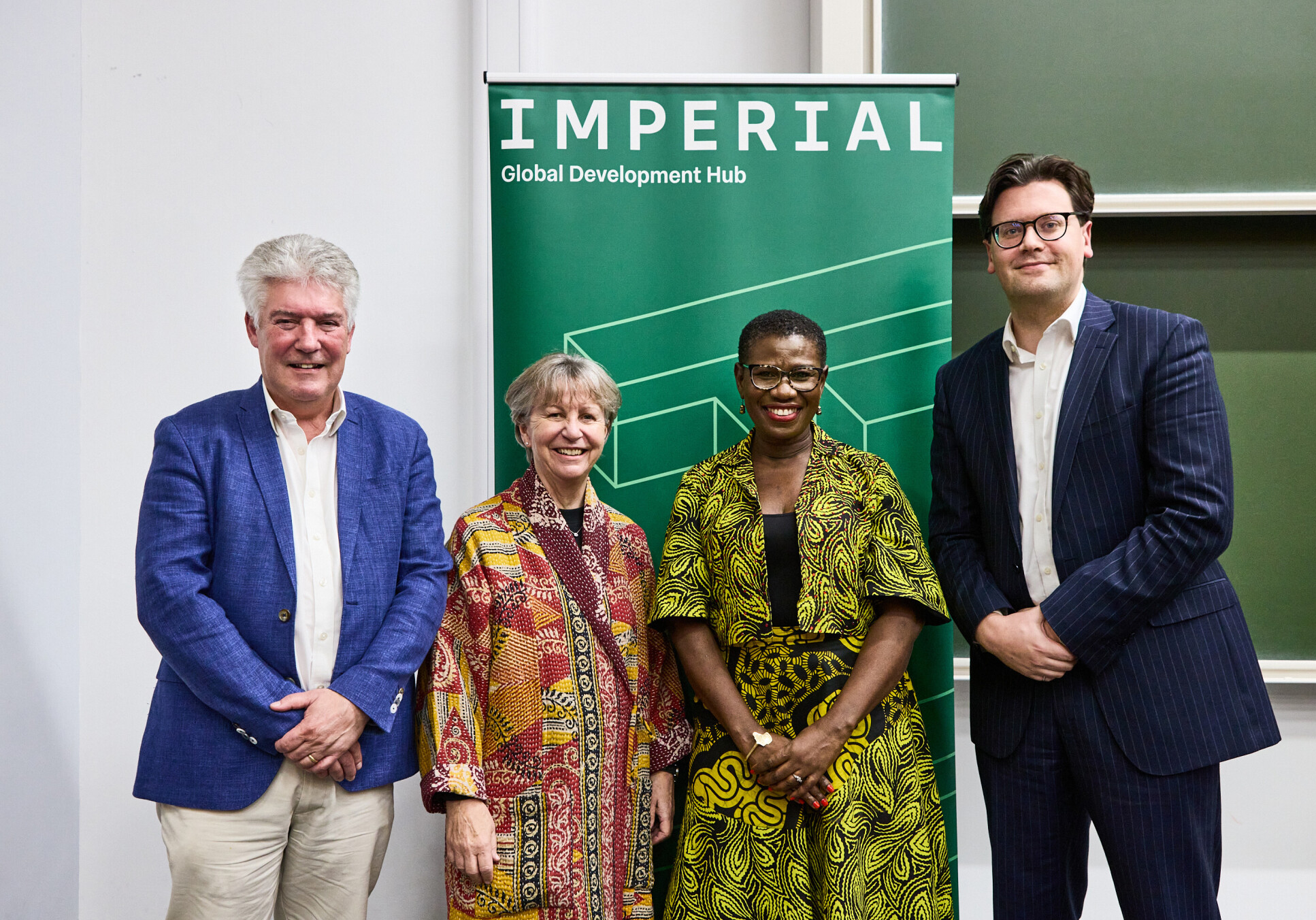 Four people stand in a line in front of a green banner reading Imperial Global Development Hub