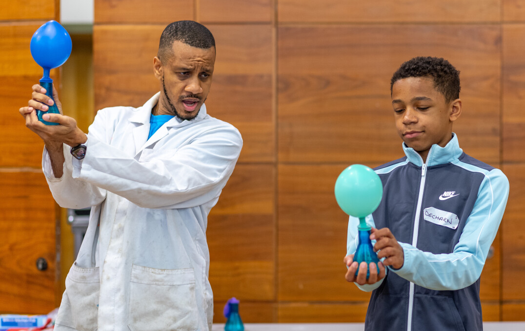 A child standing next to a scientist taking part in a demonstration using balloons