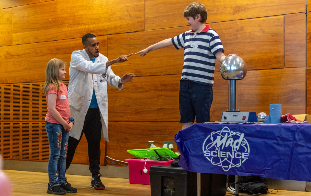 A child with their hand on a van de graaff generator next to a scientist and another child