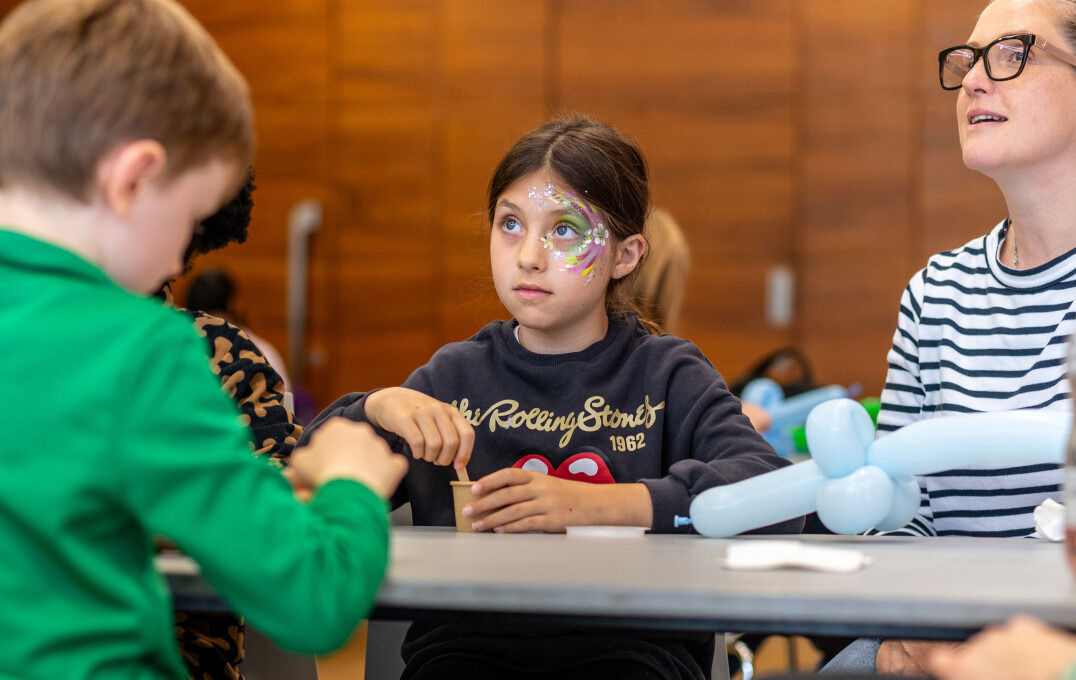 A child with their face painted sat at a table during the slime making workshop