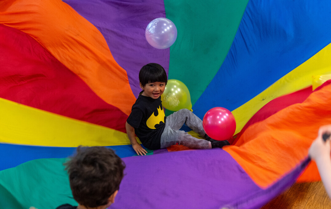 A child surrounded by balloons on a rainbow parachute