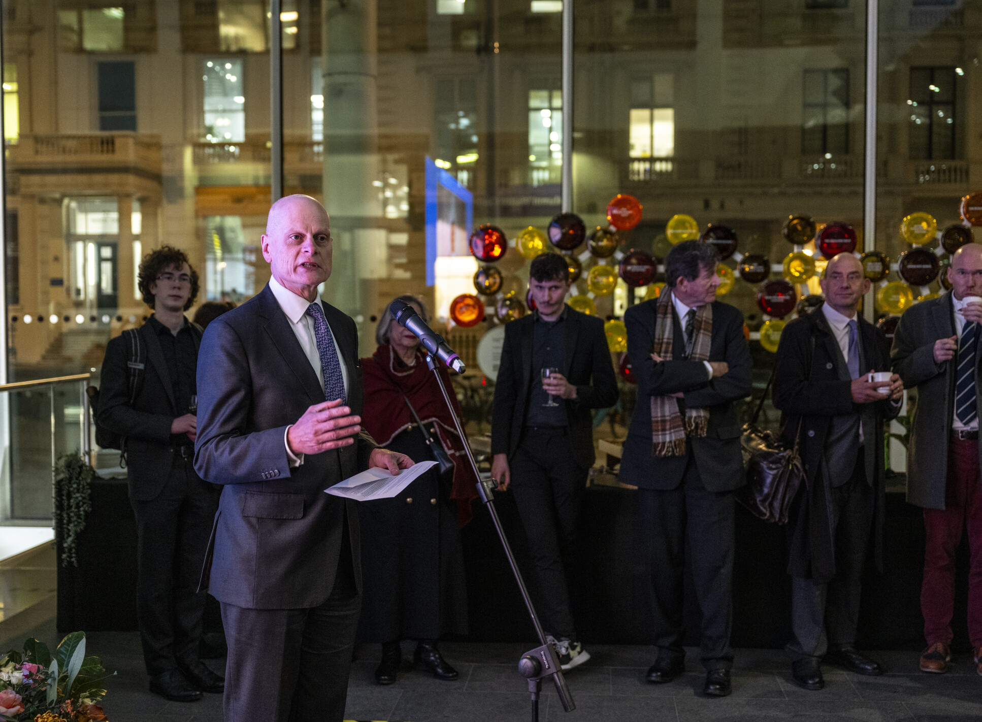 Ian Walmsley is delivering an address in front of a microphone to a reception filled with people.