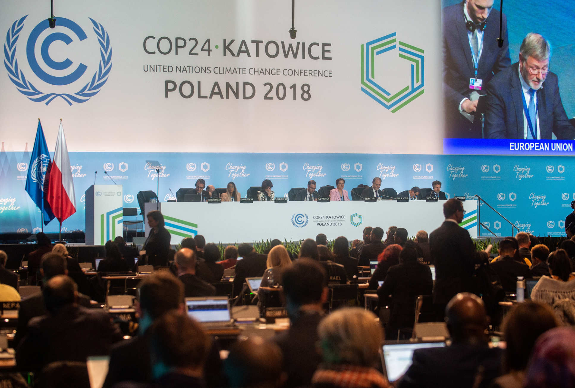 A room full of people looking towards a panel on stage with a sign behind reading "COP24 Katowice Poland 2018"