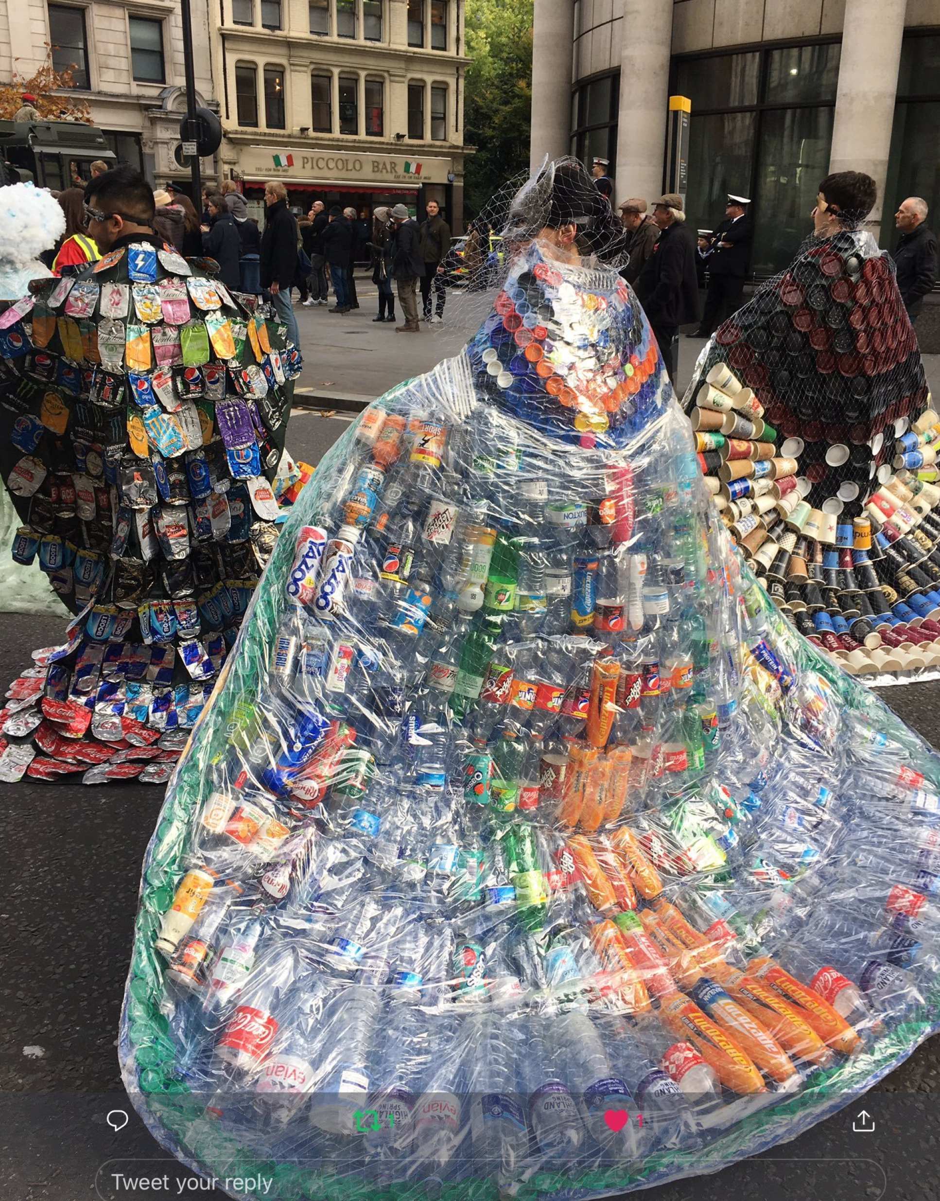 Three people wear cloaks made of trash. Left: crushed drinks cans. Centre: Plastic bottles. Right: disposable cups