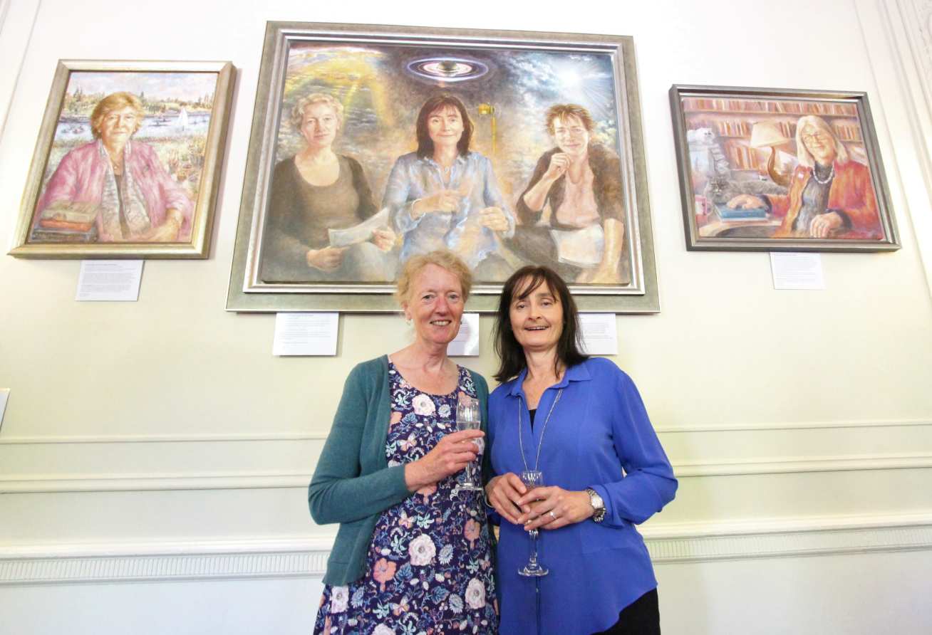 Jo Haigh and Michele Dougherty holding wine glasses in front of a painting of themselves