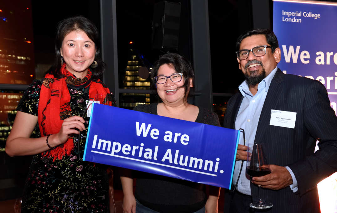 Three alumni smile at the camera in front of a view of the London skyline
