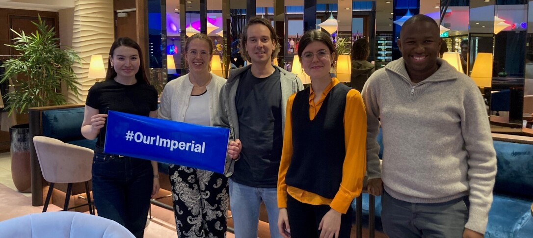 A diverse group of four alumni pictured at a past Netherlands social. They are holding up a small banner that reads '#OurImperial'. They appear to be in a restaurant or similar venue.