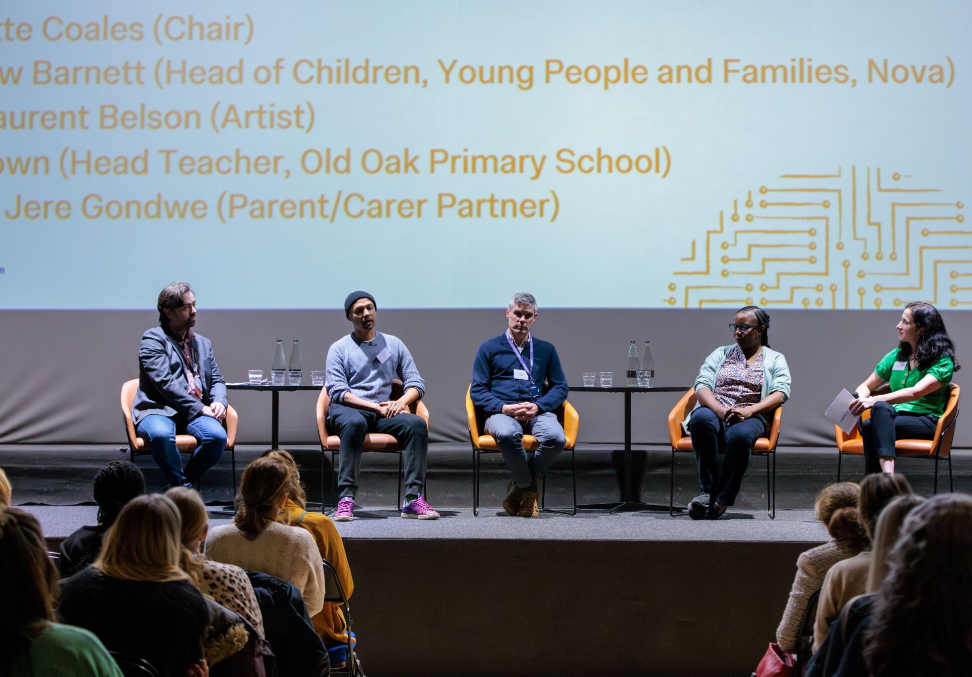 Five speakers sitting in chairs on stage