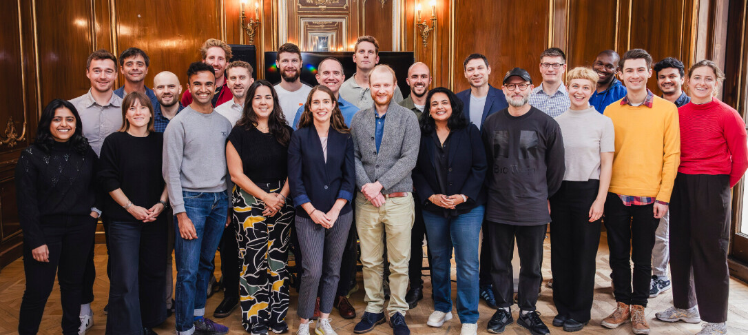 Group of people in the Better Futures Retrofit Accelerator posing in front of the camera with the backdrop of a wood-textured room and warm lights