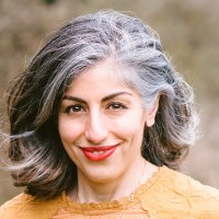 Portrait of Dr Parry Hashemi. Parry stands outside smiling, wearing an orange shirt.