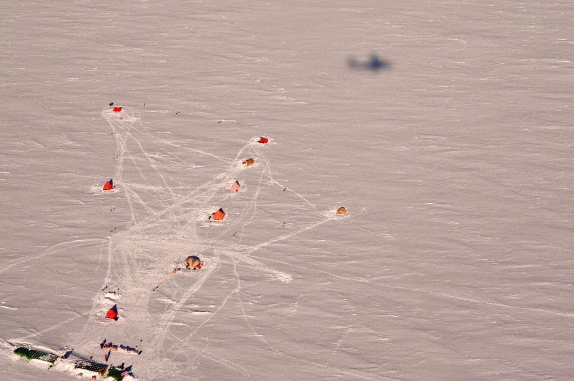 Aerial view of a small camp on an ice sheet, with the show of a plane