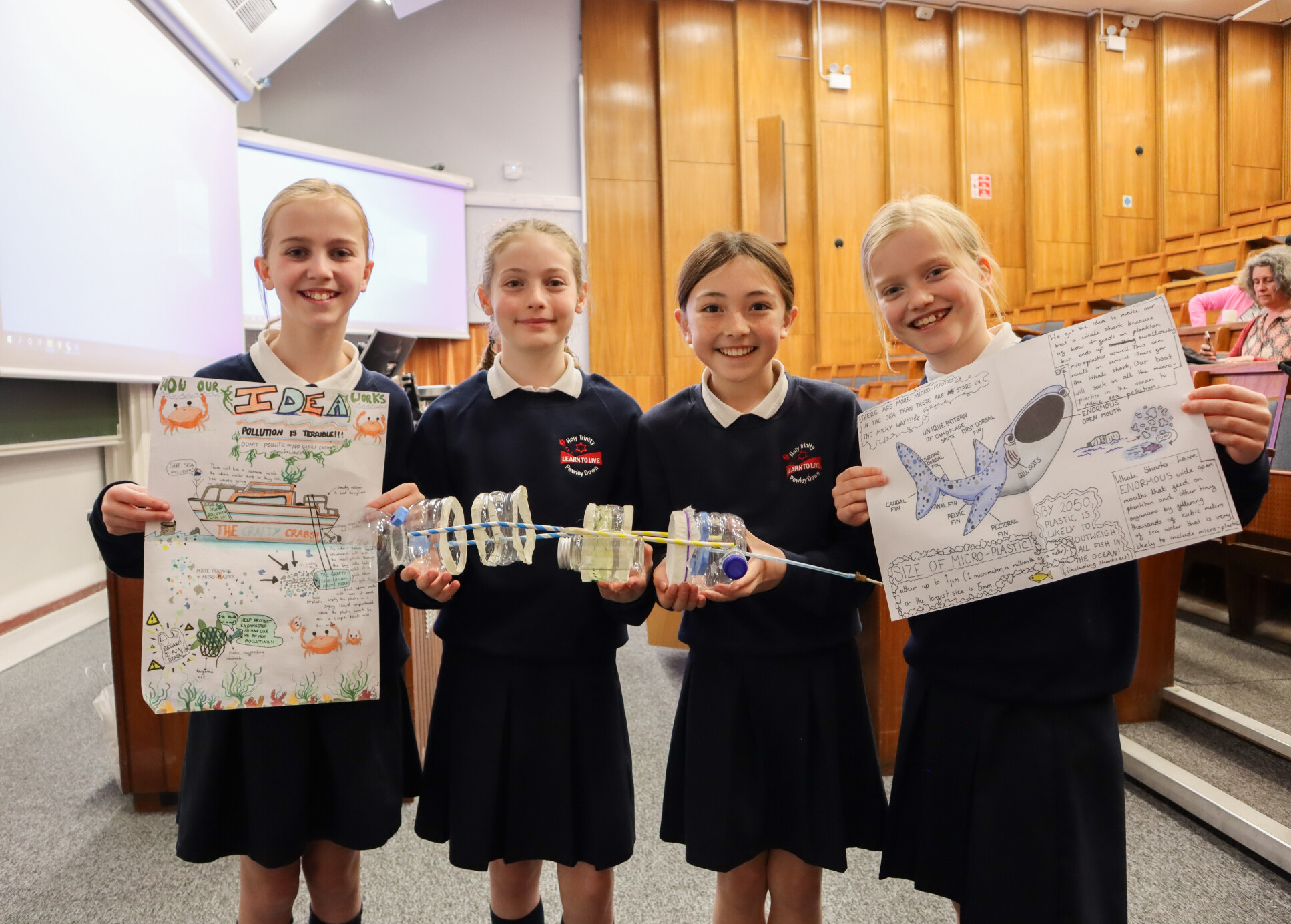 Children holding up a poster, detailing plans for a whale shark robot that can clean ocean water of microplastics.