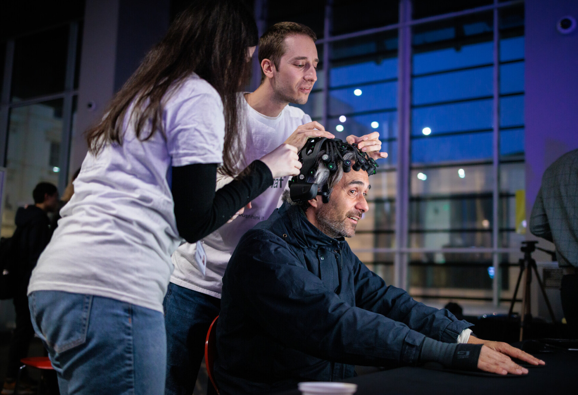 Two volunteers place headset on male visitor sitting down