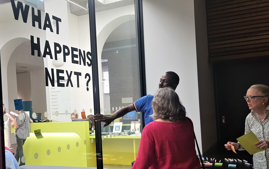 "What happens next?" in large text on a wall, with people sticking post it notes on below.