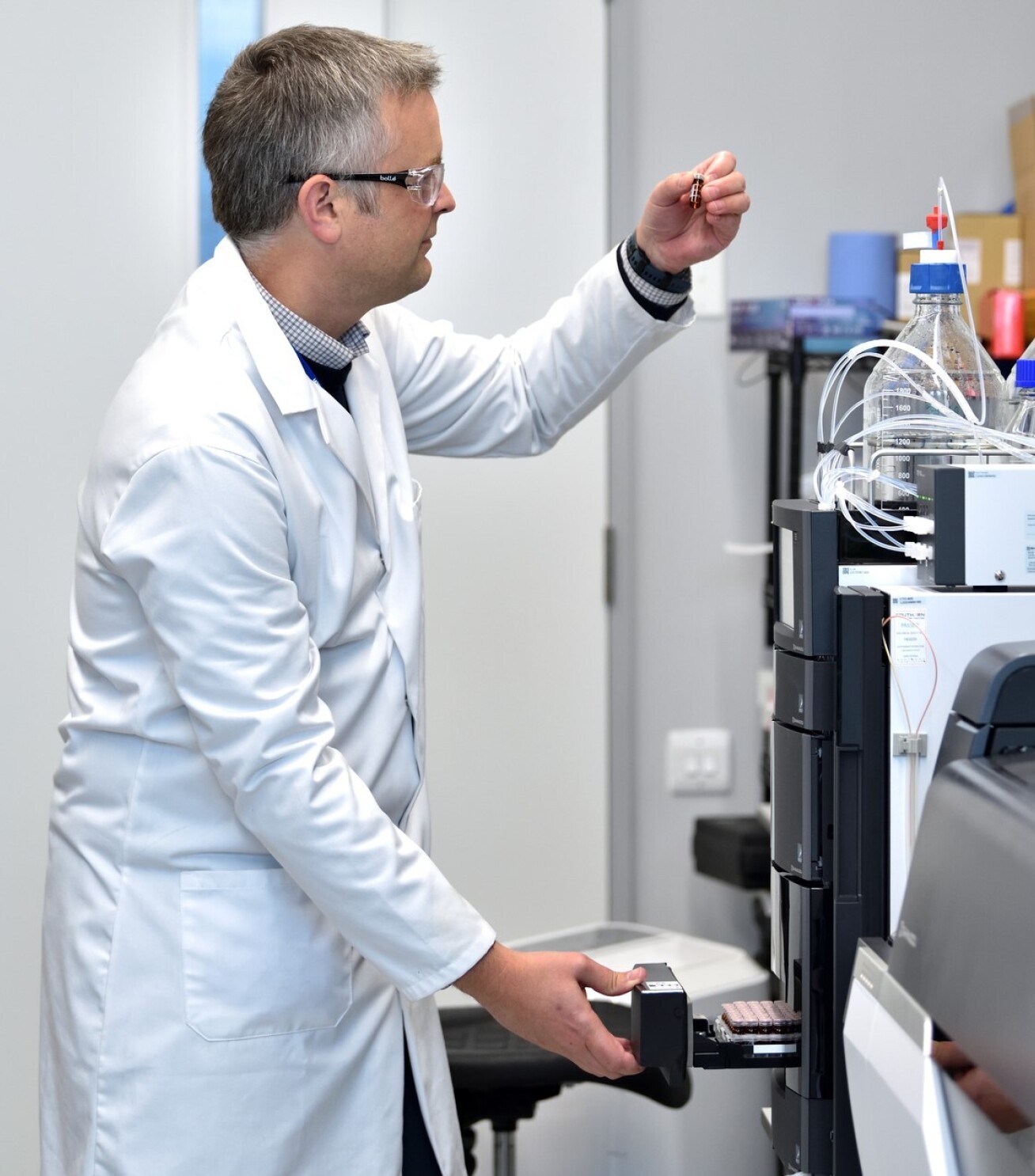 Man in a lab coat looking at a small vial in front of a machine