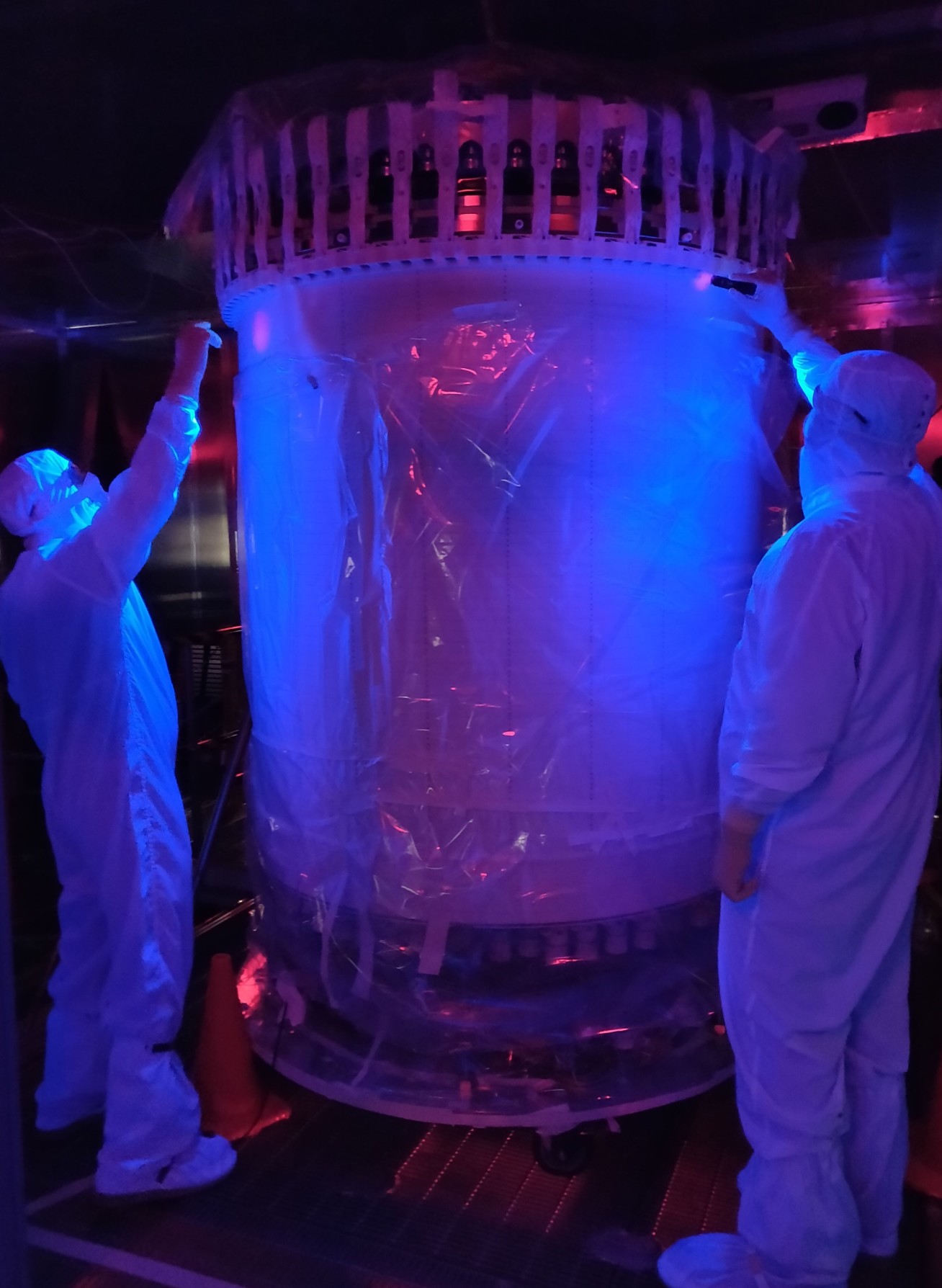 Two people in hazmat suits inspecting a large cylinder under UV light