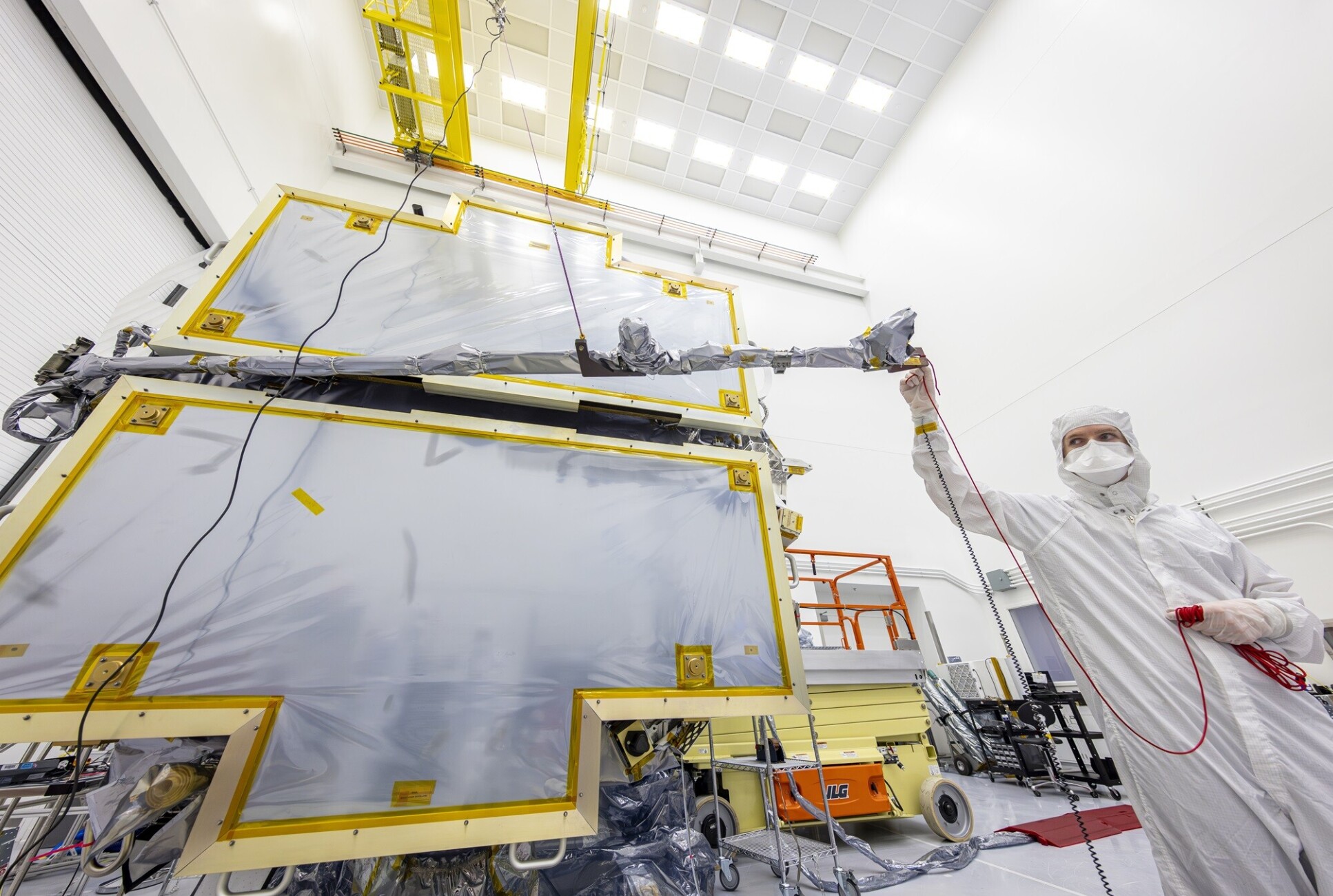 Person in a full clean suit holding a rod extending from the spacecraft