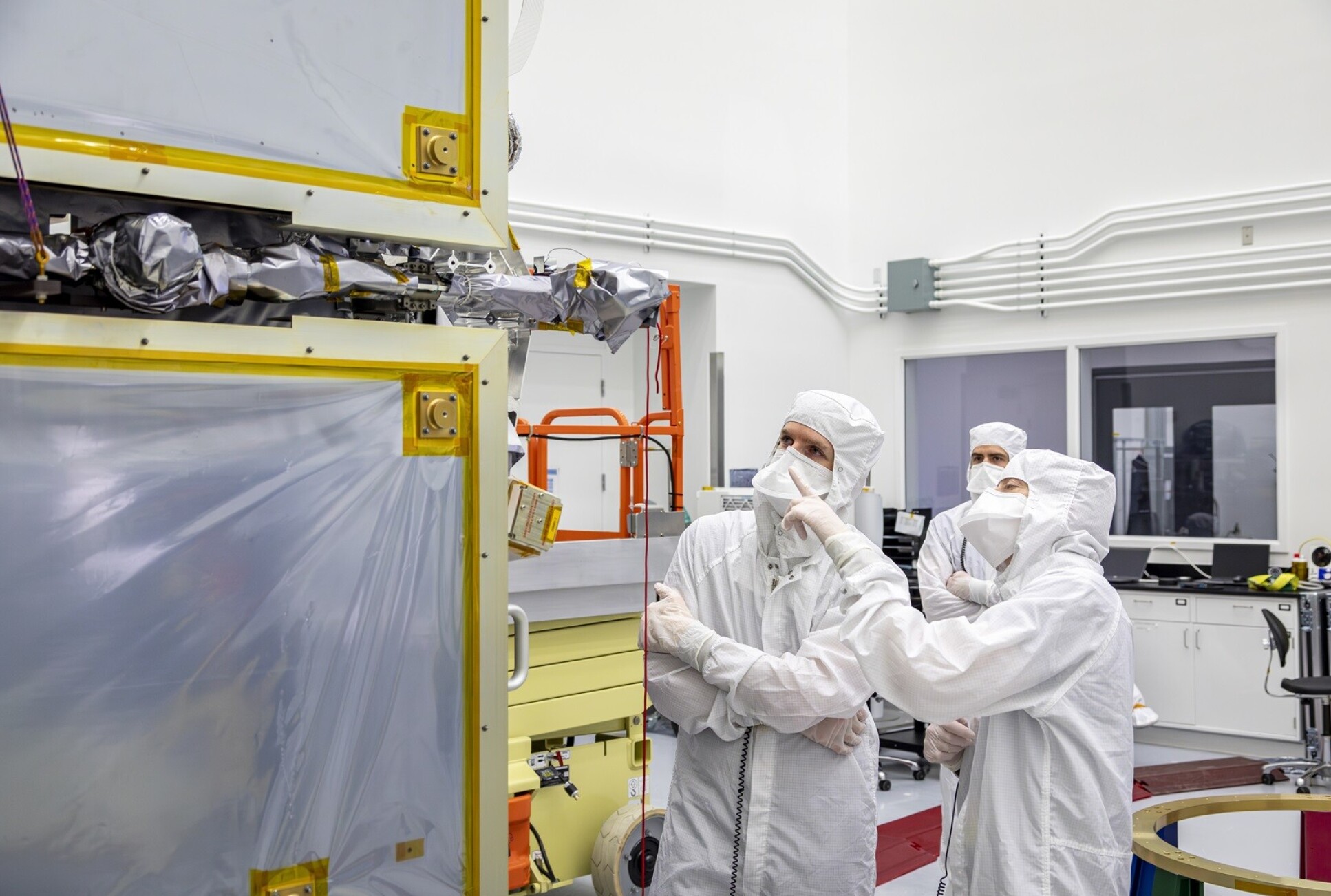 Two people in clean suits point at a corner of the spacecraft