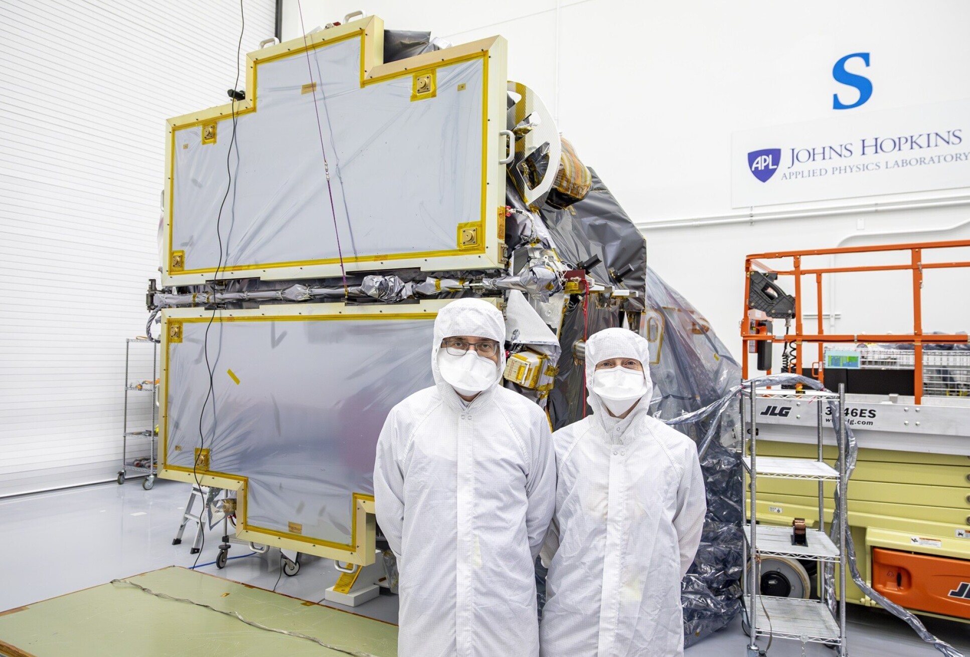 Two people in full clean suits in front of a spacecraft