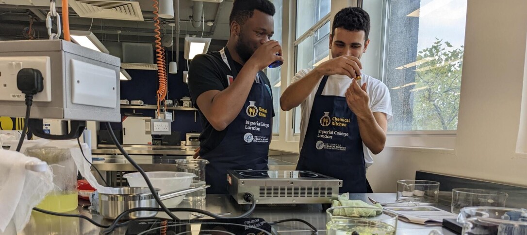 two students in a kitchen holding glassware to their face