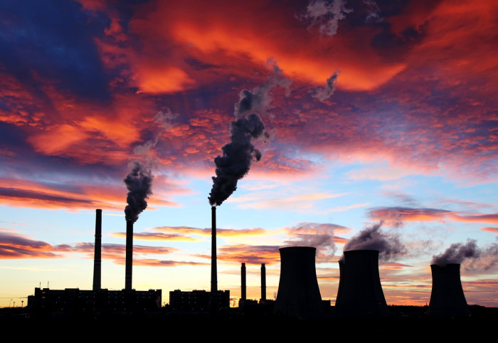 Factory pipes with smoke rising from chimneys against sunset sky