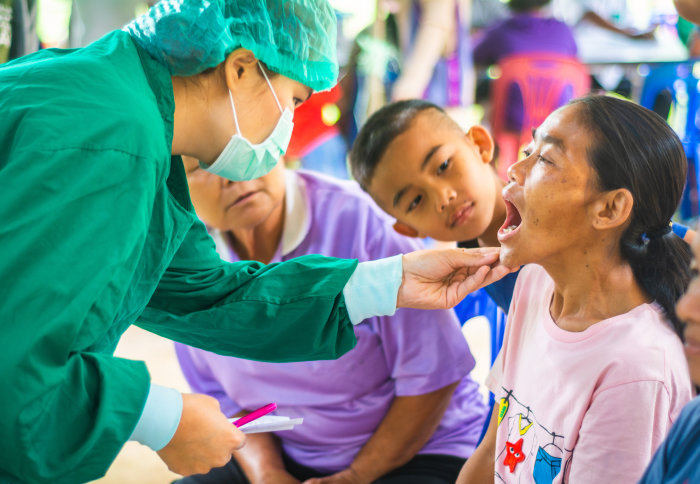 A Thai health worker looks at a woman's mouth during an examination