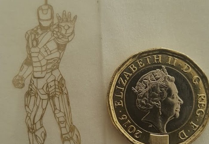 An outline image of Iron man in thin metal next to a pound coin for scale
