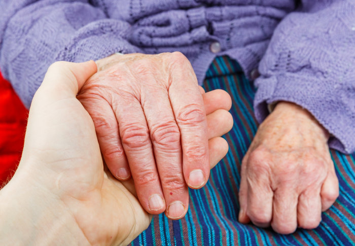 A young person holds the hand of an elderly lady