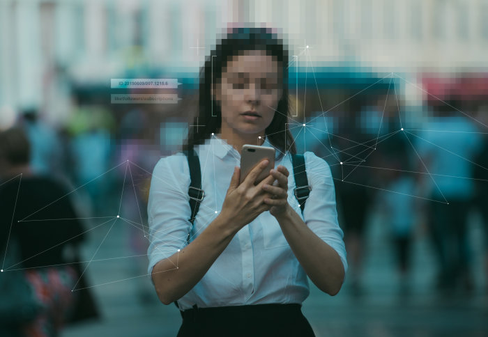 Woman with pixelated face uses smartphone with blurred out people in background