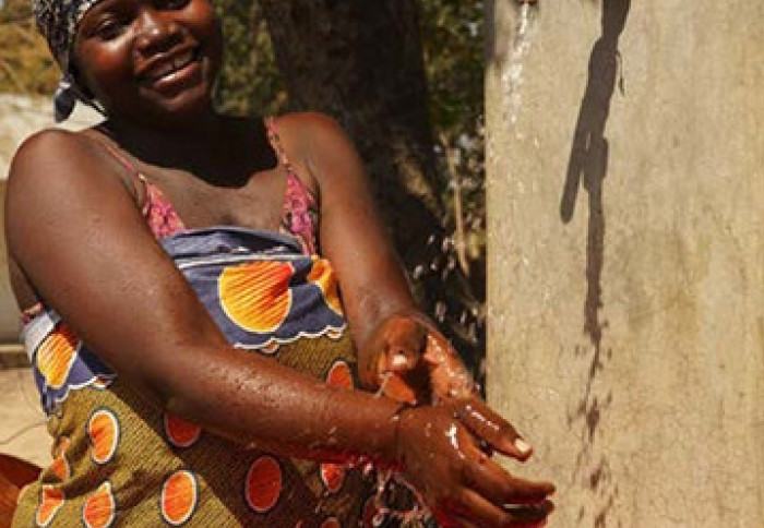 A woman washing her hands under running water in rural Mozambique