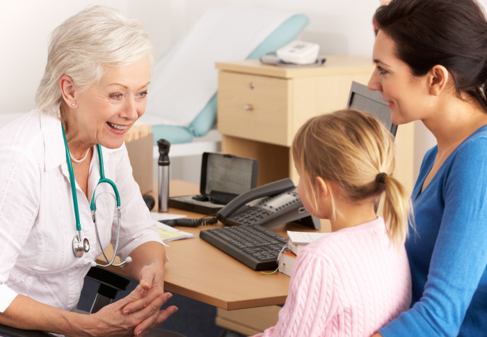 A doctor speaks to a young child and their mother.