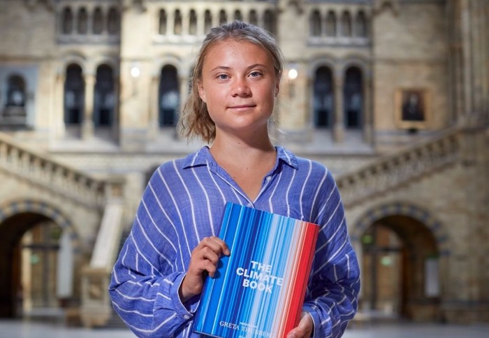 Greta Thunberg poses with her book at the Natural History Museum, the book's cover is the 'climate stripes' artwork by Dr Ed Hawkins