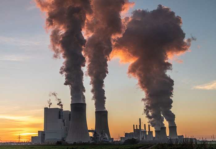 Three large concrete towers emitting smoke, with a sunset in the background