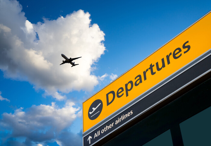 A plane flies over a departure sign