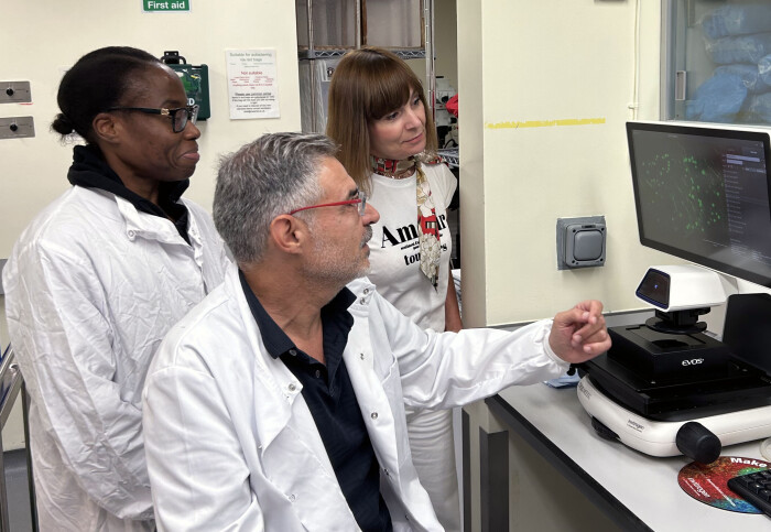 Three people in lab coats looking at a screen