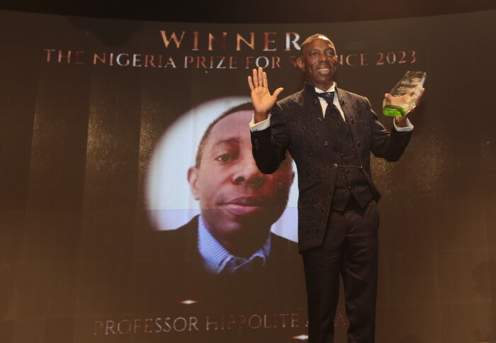 Professor Amadi stands on a stage and waves while holding his Nigeria Prize for Science