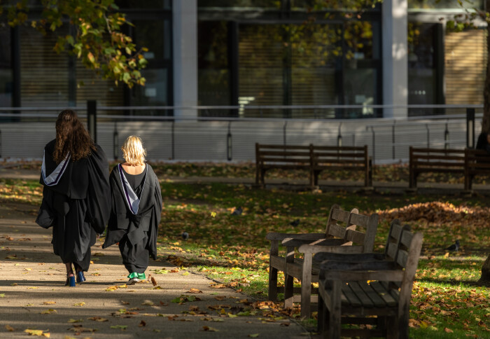 Two students in graduation robes walking away from the camera
