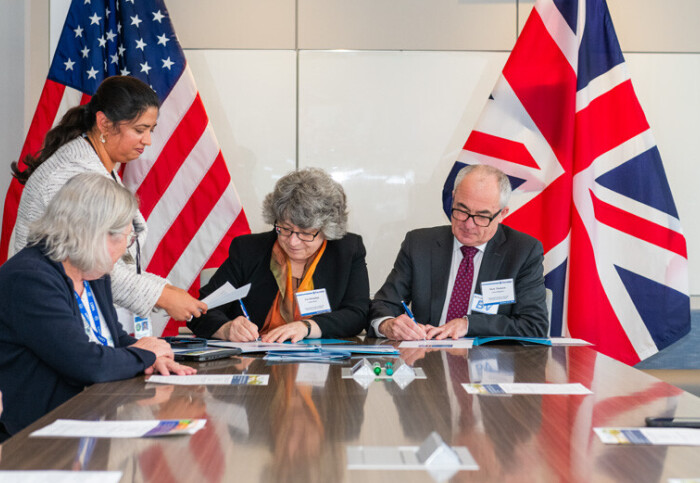 People signing documents in front of US and UK flags